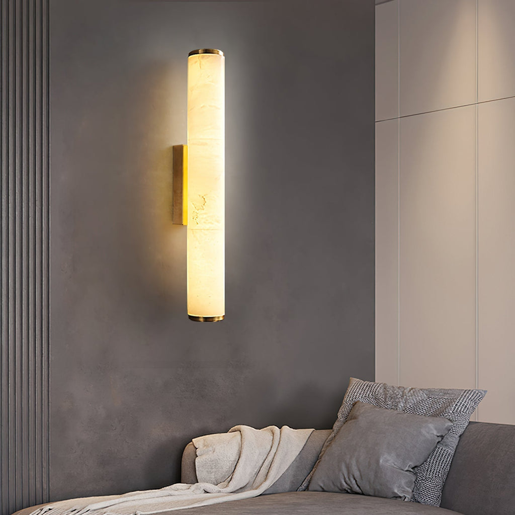 Clérachic brass sconce against a fluted concrete-grey wall, lighting a daybed dressed in linen and grey cushions.