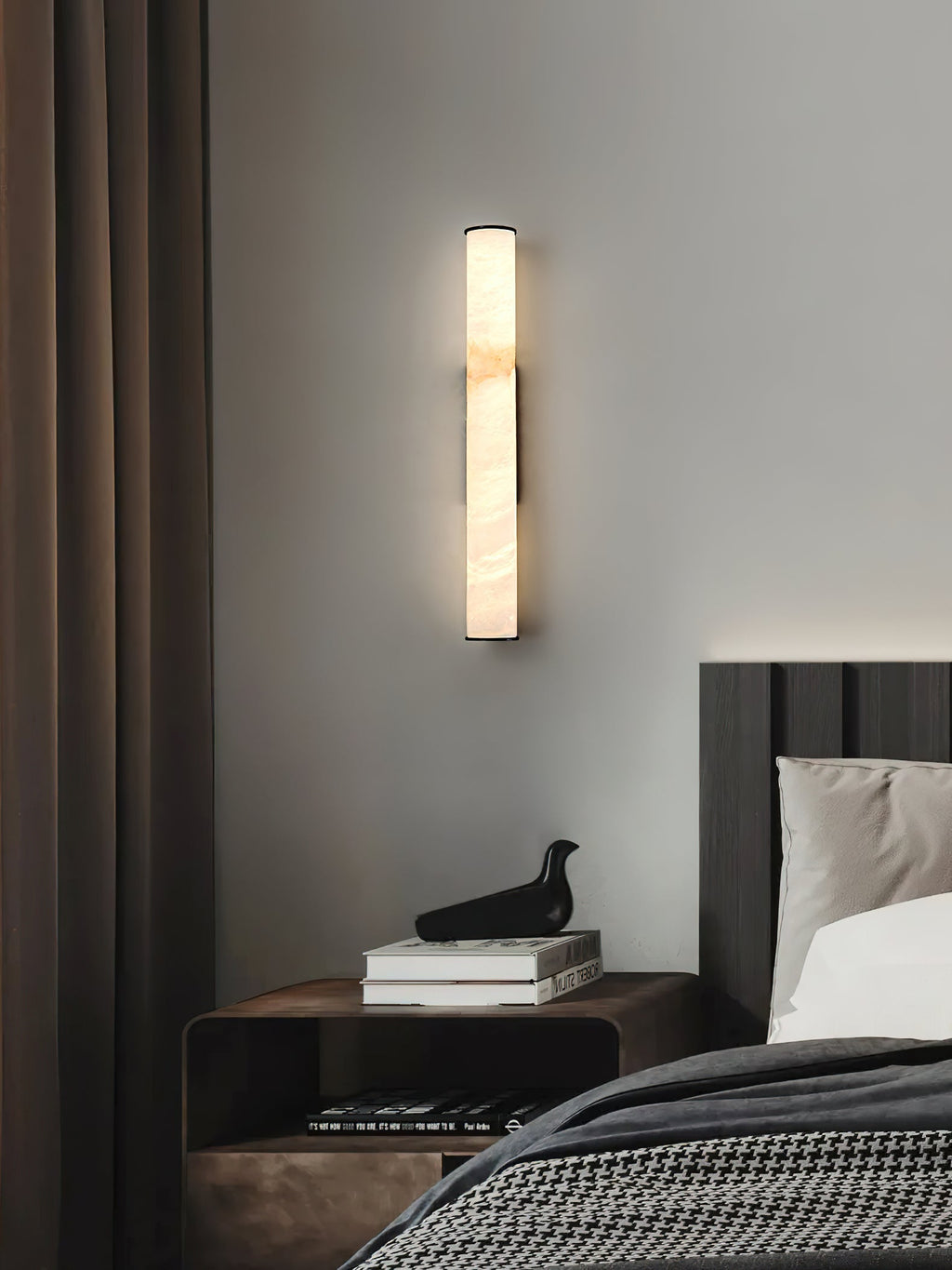 Clérachic alabaster sconce at bedside, its warm column lifting a corner of books, curtains and a small bird figure.
