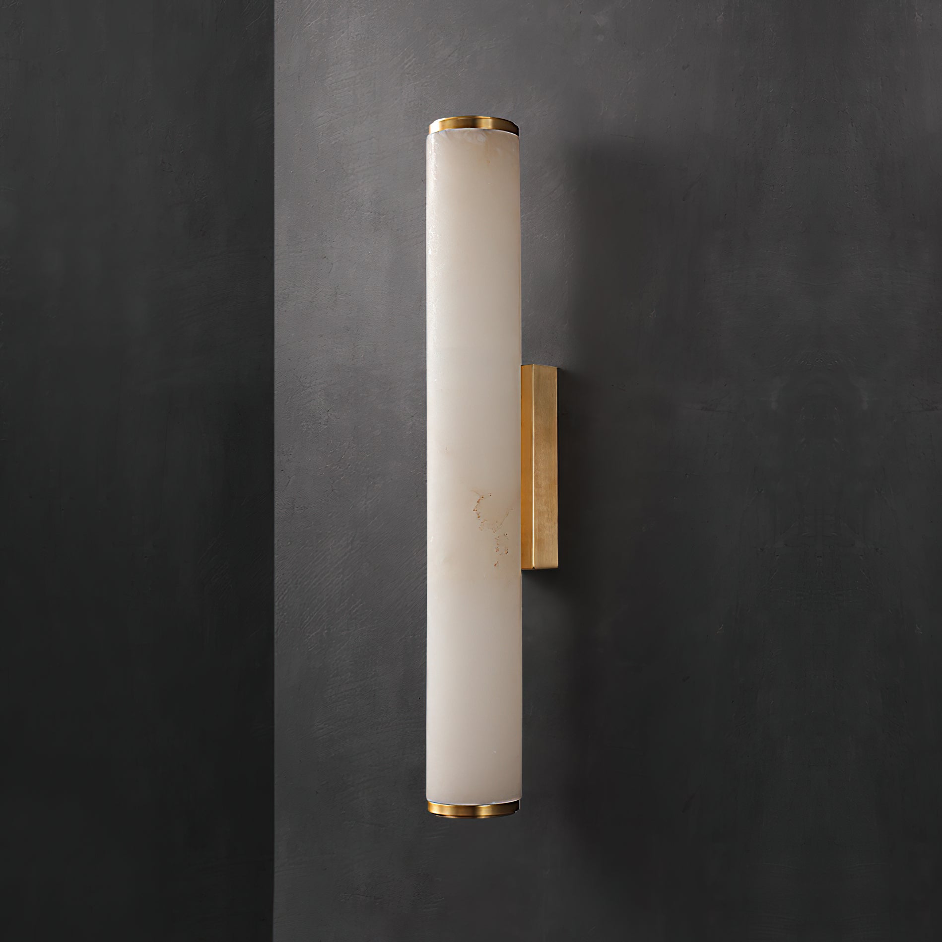 Clérachic alabaster sconce unlit on a dark charcoal wall, the brass bracket reading as a bright vertical line.