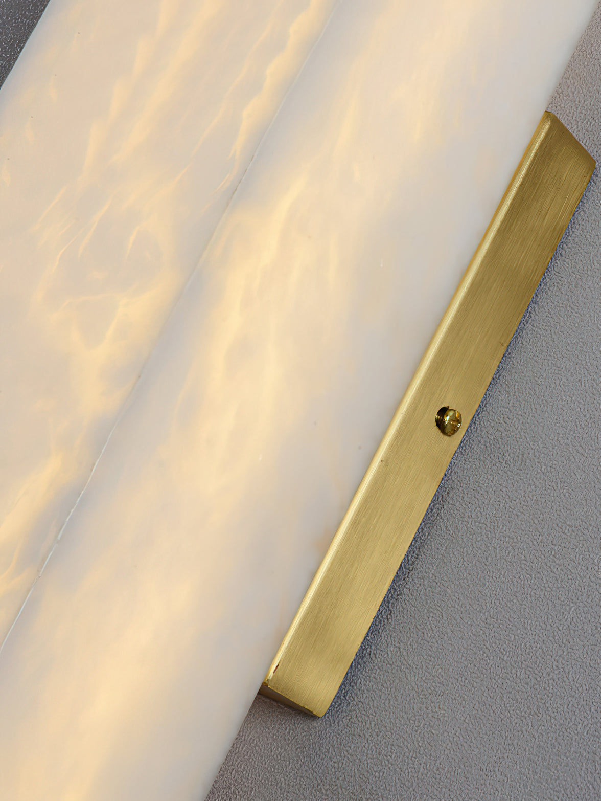 Close view of the Clérachic sconce's brushed brass mounting bar and fixing screw meeting the alabaster edge.