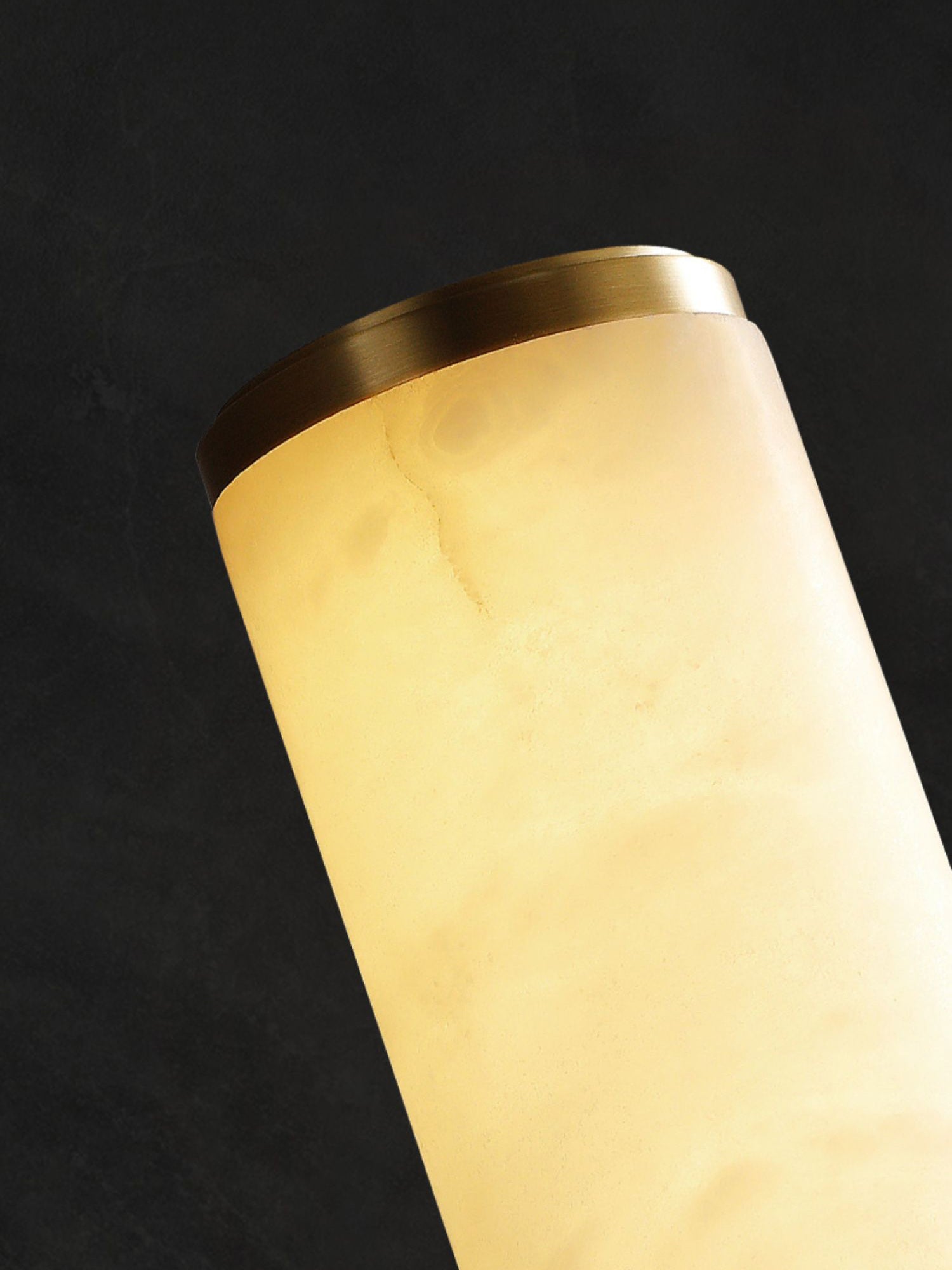 Detail of the Clérachic sconce's brass end collar, capping the softly lit alabaster cylinder.