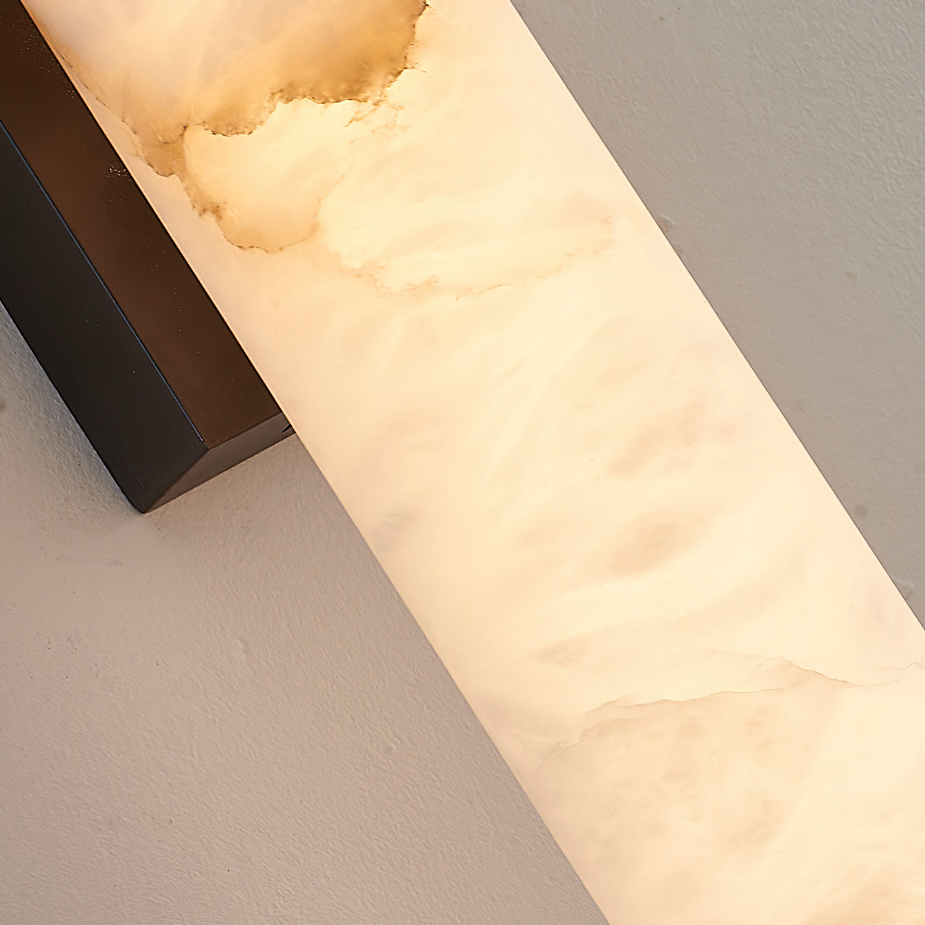 Macro of the Clérachic sconce's alabaster panel, honey-toned veining running beside the bronze bracket.