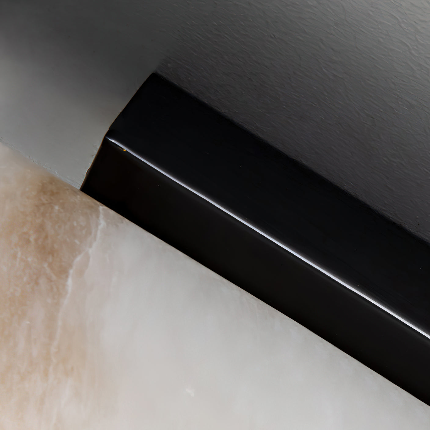 Close crop of the Clérachic sconce's glossy black bracket where it meets the translucent alabaster face.