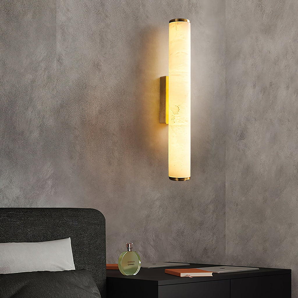 Clérachic brass sconce on a grey plaster wall, warming a bedside table with books and a glass bottle.