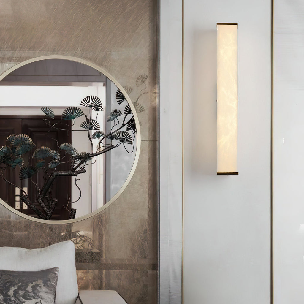 Clérachic sconce beside a round decorative mirror, its slim lit column set on a pale panelled wall.