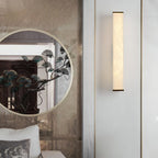 Clérachic sconce beside a round decorative mirror, its slim lit column set on a pale panelled wall.