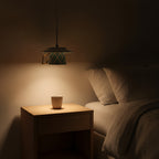 Clérachic argyle teacup pendant lit beside a bed at night, its light passing straight down onto a bare oak nightstand