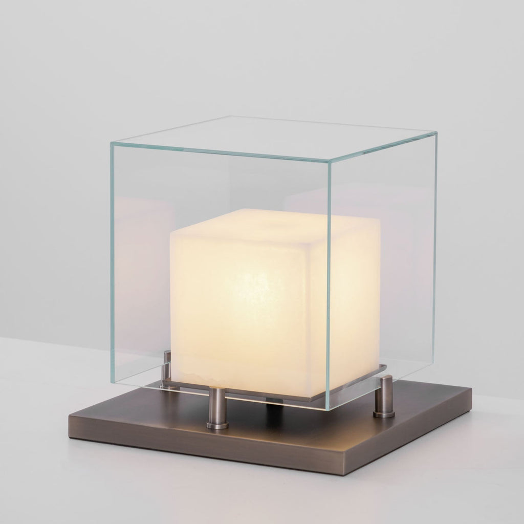 Clérachic Arqra alabaster table lamp lit on a dark surface, glass dome glowing above its metal base.