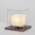 Clérachic Arqra alabaster table lamp lit on a dark surface, glass dome glowing above its metal base.