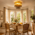 Amber art glass Clérachic flush mount glowing above a round breakfast table in a bay-windowed nook with cane chairs and sheer curtains.