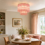 Pink Clérachic flush mount above a round table with pink cushions and a vase of wildflowers, with a gold-framed print on the wall.