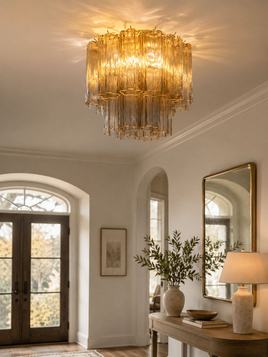 Amber-toned Clérachic flush mount at the top of a hallway with arched doors, a gilt mirror and a lamp on a console table.