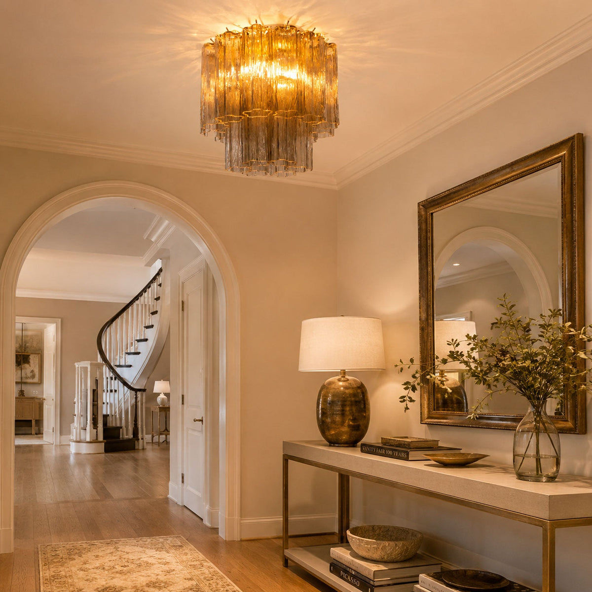 Amber glass Clérachic flush mount glowing over an archway and a hall console, beside a gilt-framed mirror and a brass table lamp.