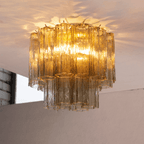 Looking up at the amber glass tubes of this Clérachic flush mount, lit from inside and throwing patterns of light across the ceiling.