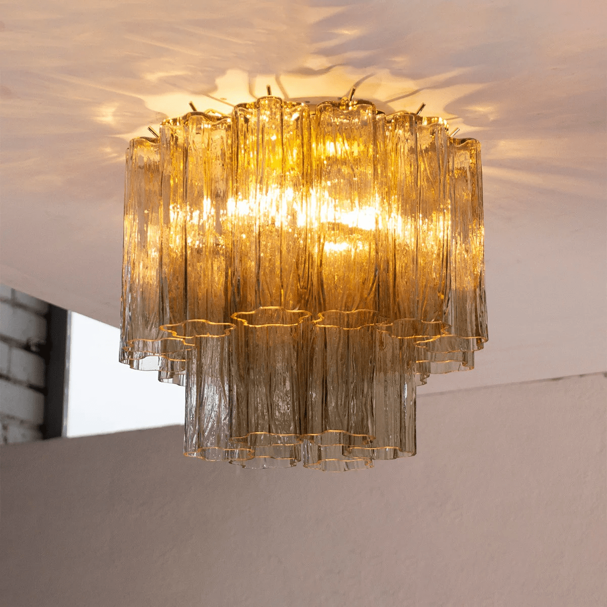 Looking up at the amber glass tubes of this Clérachic flush mount, lit from inside and throwing patterns of light across the ceiling.