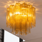 Looking up at the amber art glass tubes of this Clérachic flush mount, lit and casting warm shadows on the ceiling.