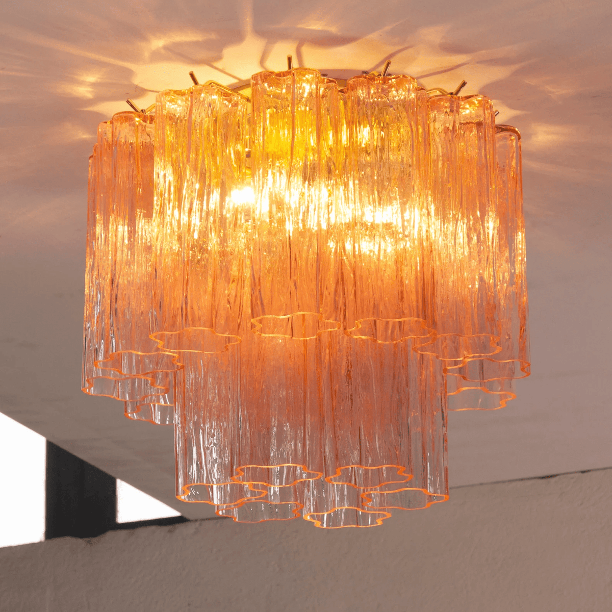 Looking up at the pink and apricot glass tubes of this Clérachic flush mount, lit from within and reflecting on the ceiling.