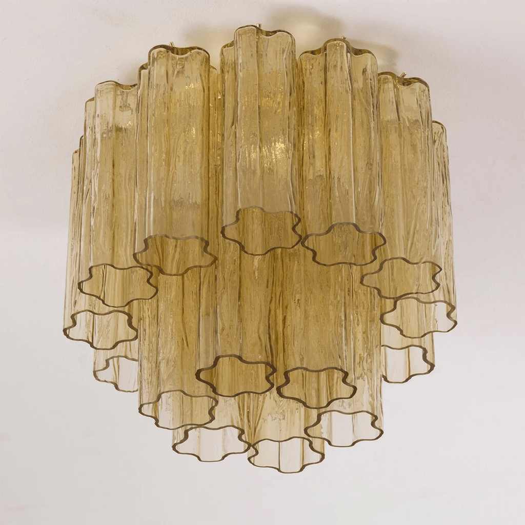Looking up at the amber-gold glass tubes of this Clérachic flush mount, with their star-shaped ends and brass-toned fittings.