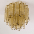 Looking up at the amber-gold glass tubes of this Clérachic flush mount, with their star-shaped ends and brass-toned fittings.