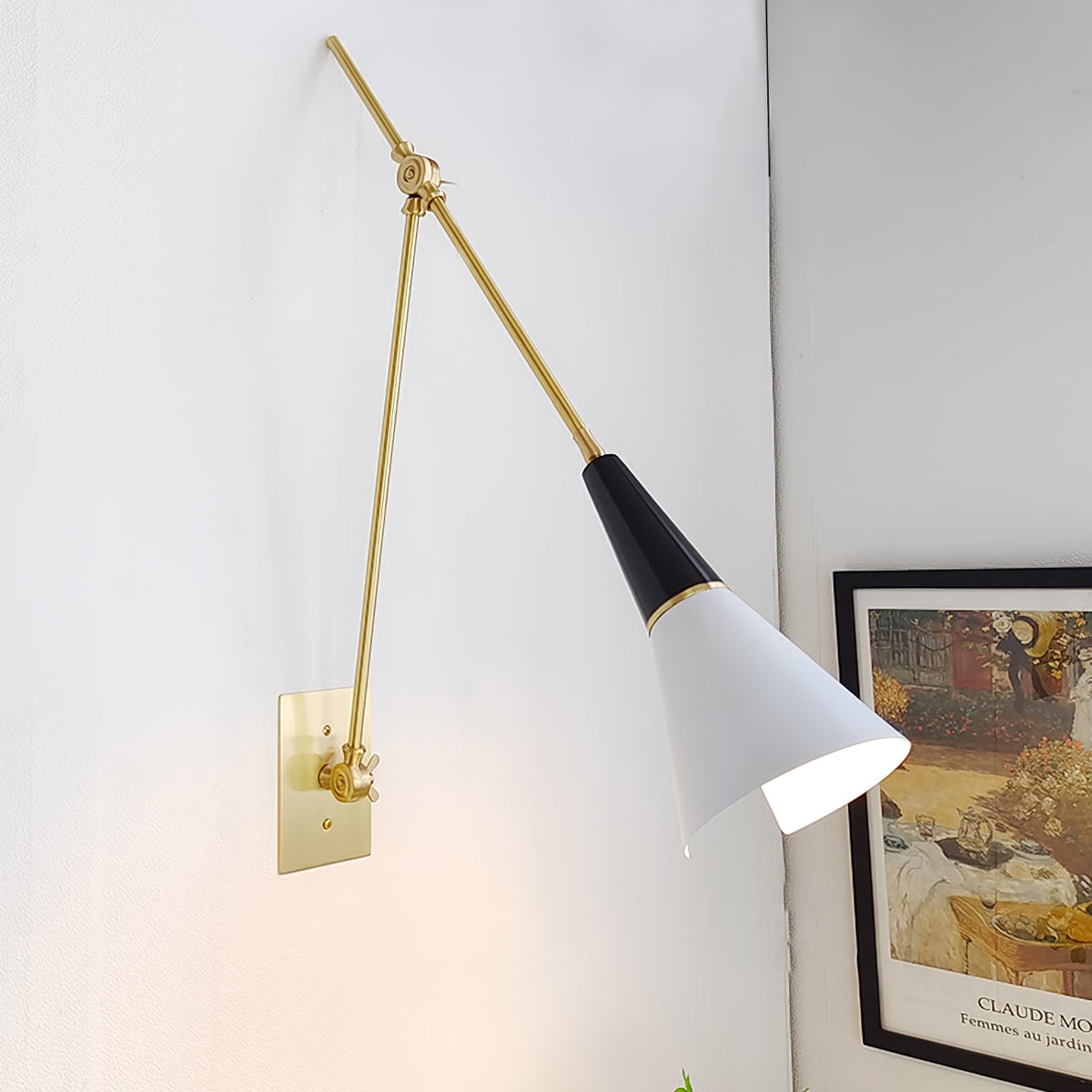 Clérachic wall light with a white cone shade swung out from its brass arms, beside a framed Impressionist print on a pale wall.