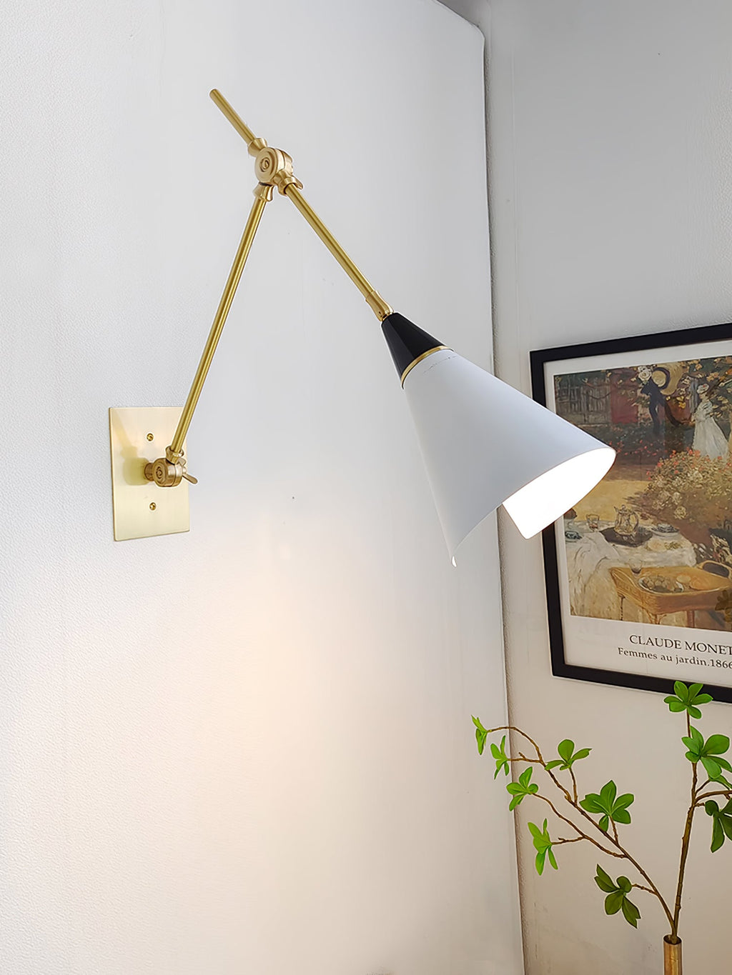 Clérachic wall light with its arm angled out over a pale corner, the white cone shade turned towards a framed garden print and a green branch.