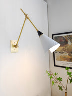 Clérachic wall light with its arm angled out over a pale corner, the white cone shade turned towards a framed garden print and a green branch.
