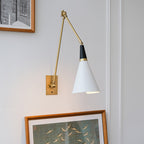 Clérachic wall light with a white cone shade on a folded brass arm, above a framed painting of birds on a pale wall.