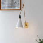 Clérachic wall light with its arm folded close, the white cone shade hanging below the joint beside a framed print and white flowers.