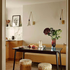 Two Clérachic wall lights on a cream wall above a dining table with a vase of dark flowers, in a corner with marble shelving.