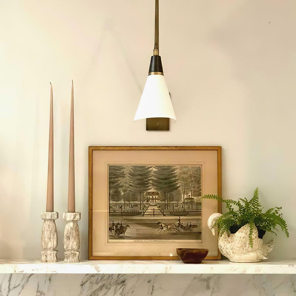 Clérachic wall light with a white cone shade and black neck above a marble ledge with tall taper candles and a framed print.