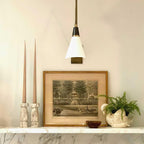 Clérachic wall light with a white cone shade and black neck above a marble ledge with tall taper candles and a framed print.
