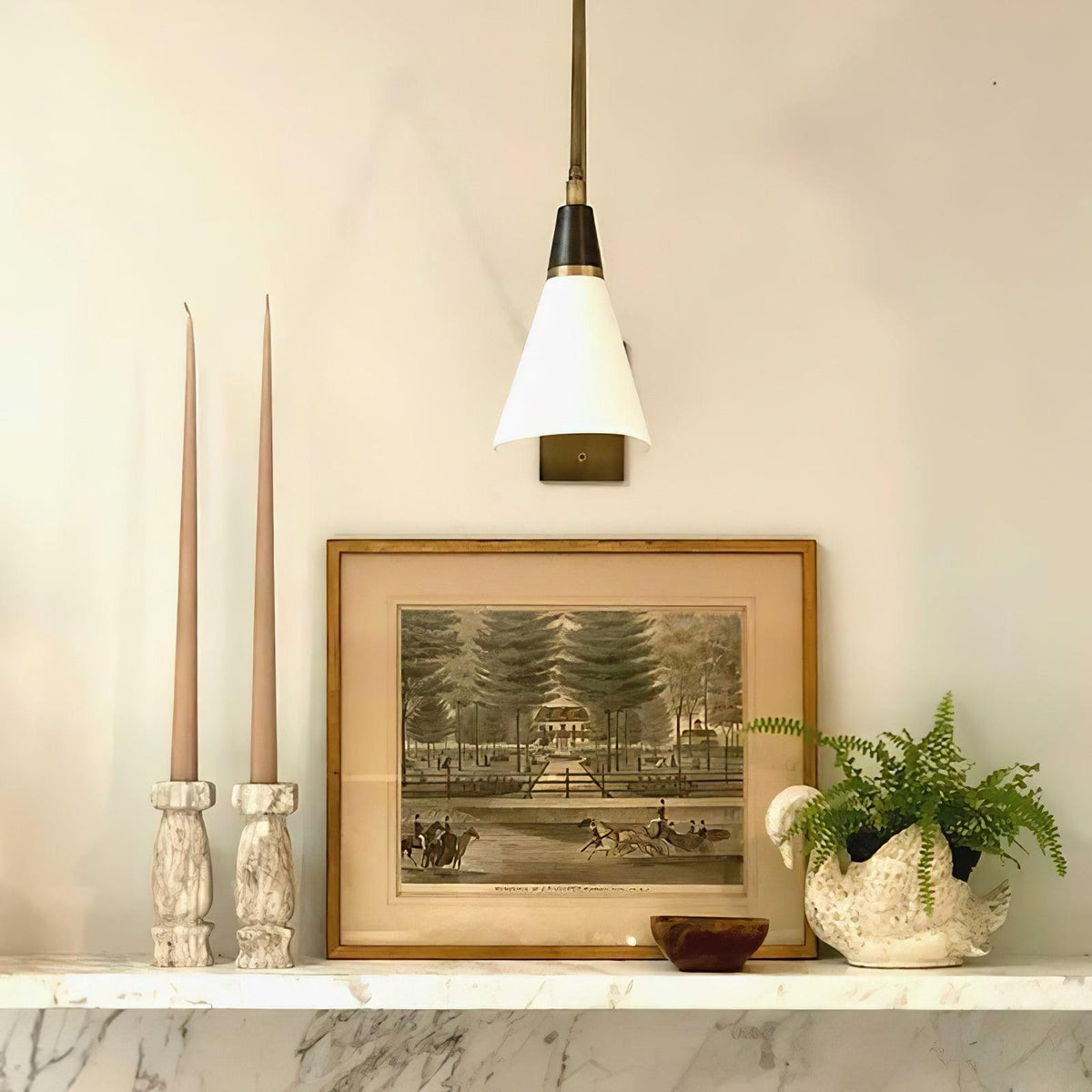 Clérachic wall light with a white cone shade and black neck above a marble ledge with tall taper candles and a framed print.
