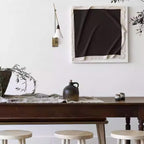 Clérachic wall light with a white cone shade beside a large black-and-cream artwork, above a dark wooden table with stools.