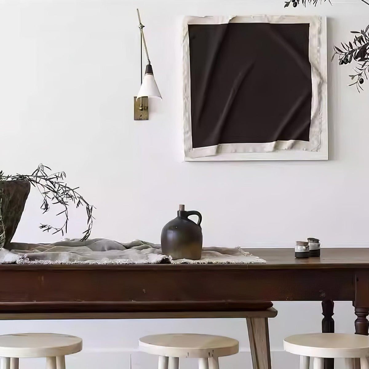 Clérachic wall light with a white cone shade beside a large black-and-cream artwork, above a dark wooden table with stools.