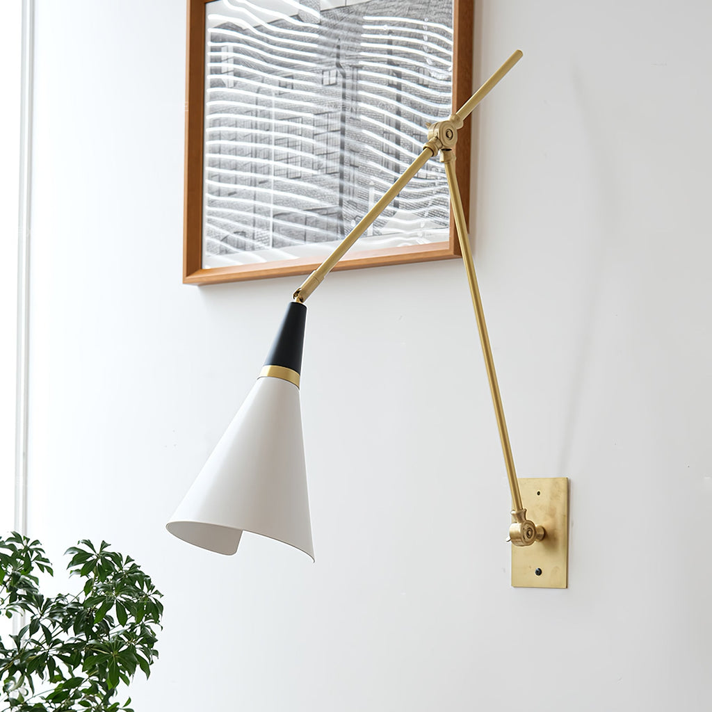 Close, angled view of a Clérachic wall light with a white cone shade and brass arms reaching across a white wall by a framed print.