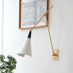 Close, angled view of a Clérachic wall light with a white cone shade and brass arms reaching across a white wall by a framed print.