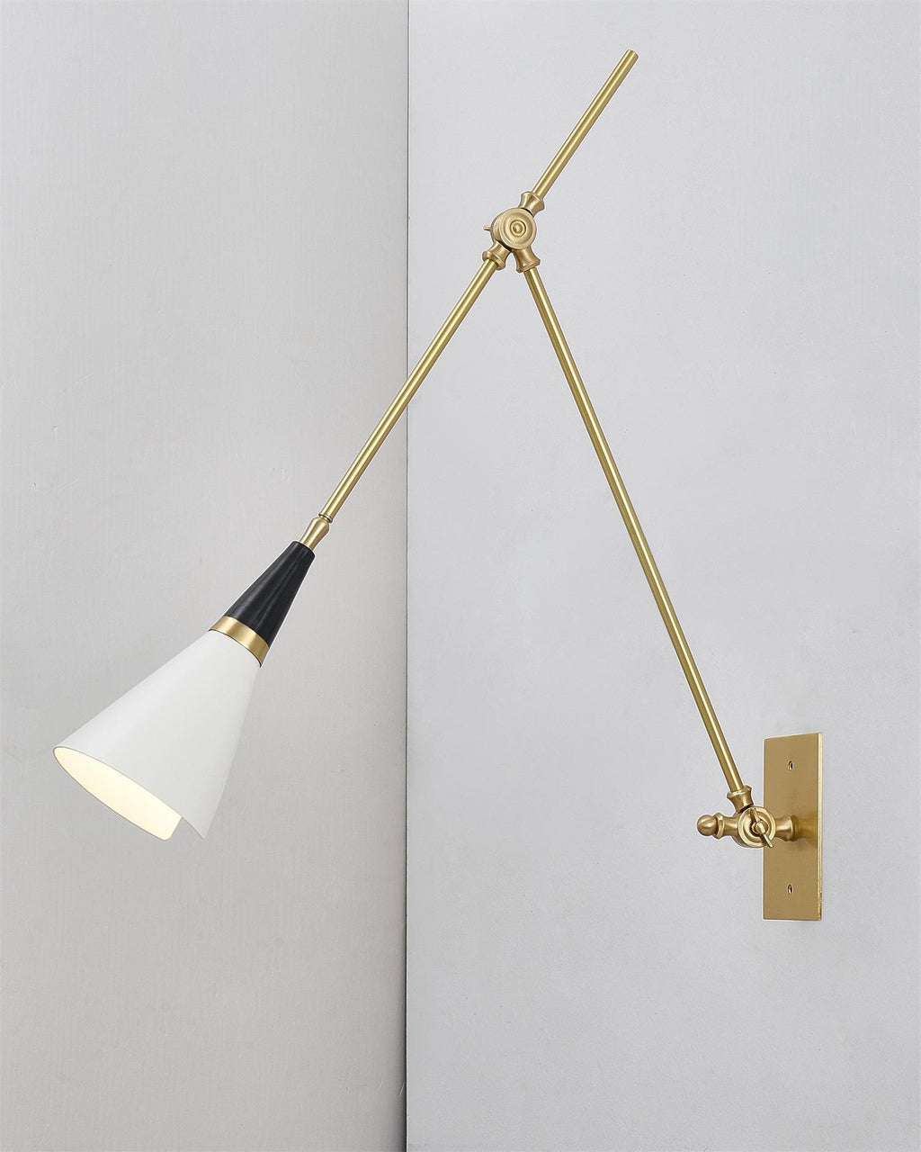 Clérachic wall light with its white cone shade turned down, mounted on a pale wall in a plain corner with a brass backplate.