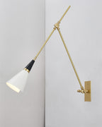 Clérachic wall light with its white cone shade turned down, mounted on a pale wall in a plain corner with a brass backplate.