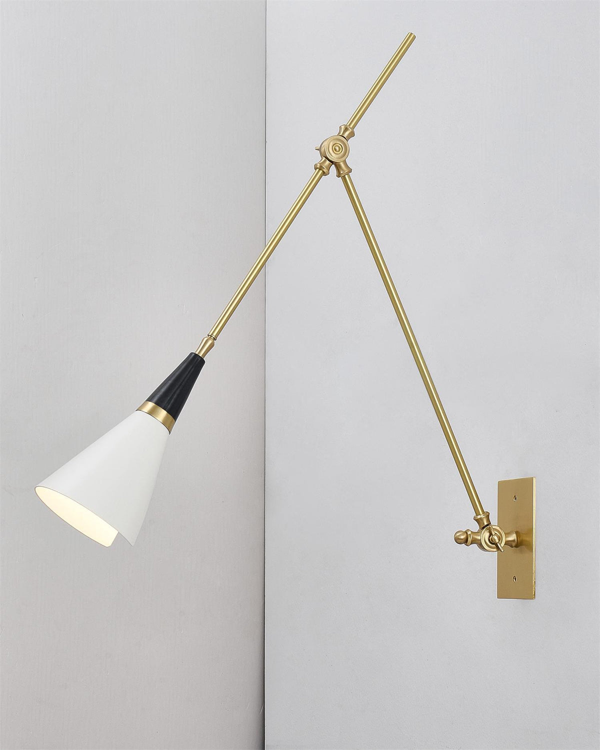Clérachic wall light with its white cone shade turned down, mounted on a pale wall in a plain corner with a brass backplate.