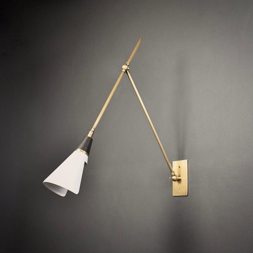 Clérachic wall light on a dark grey wall, with a white cone shade, a black neck and two brass arms reaching up from the backplate.