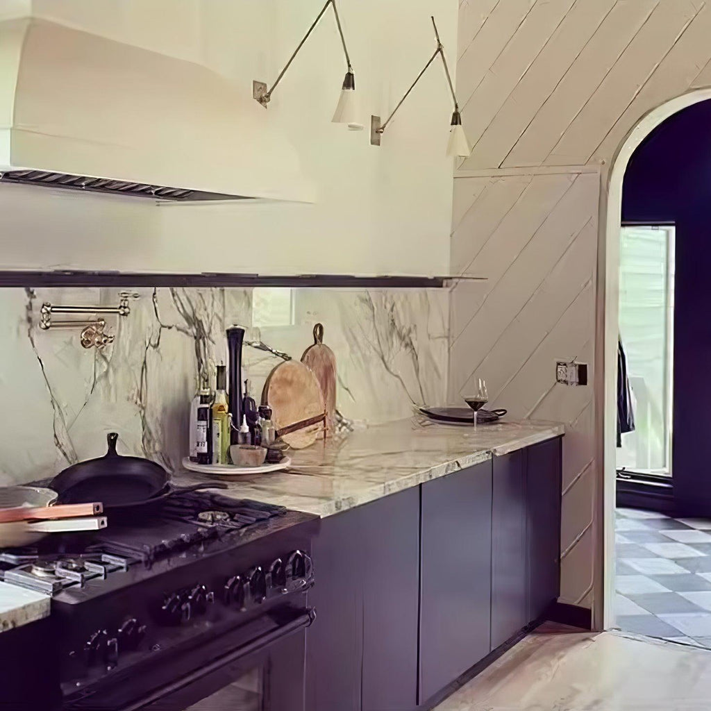 Two Clérachic wall lights with cone shades above a kitchen range and marble splashback, beside an arched doorway and a chequered floor.