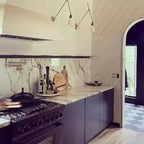Two Clérachic wall lights with cone shades above a kitchen range and marble splashback, beside an arched doorway and a chequered floor.