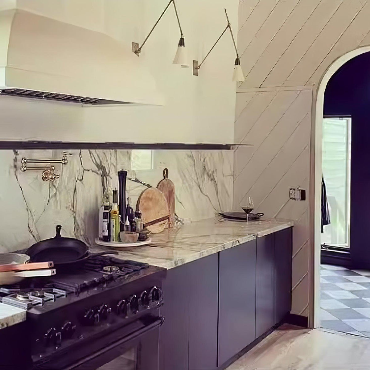 Two Clérachic wall lights with cone shades above a kitchen range and marble splashback, beside an arched doorway and a chequered floor.