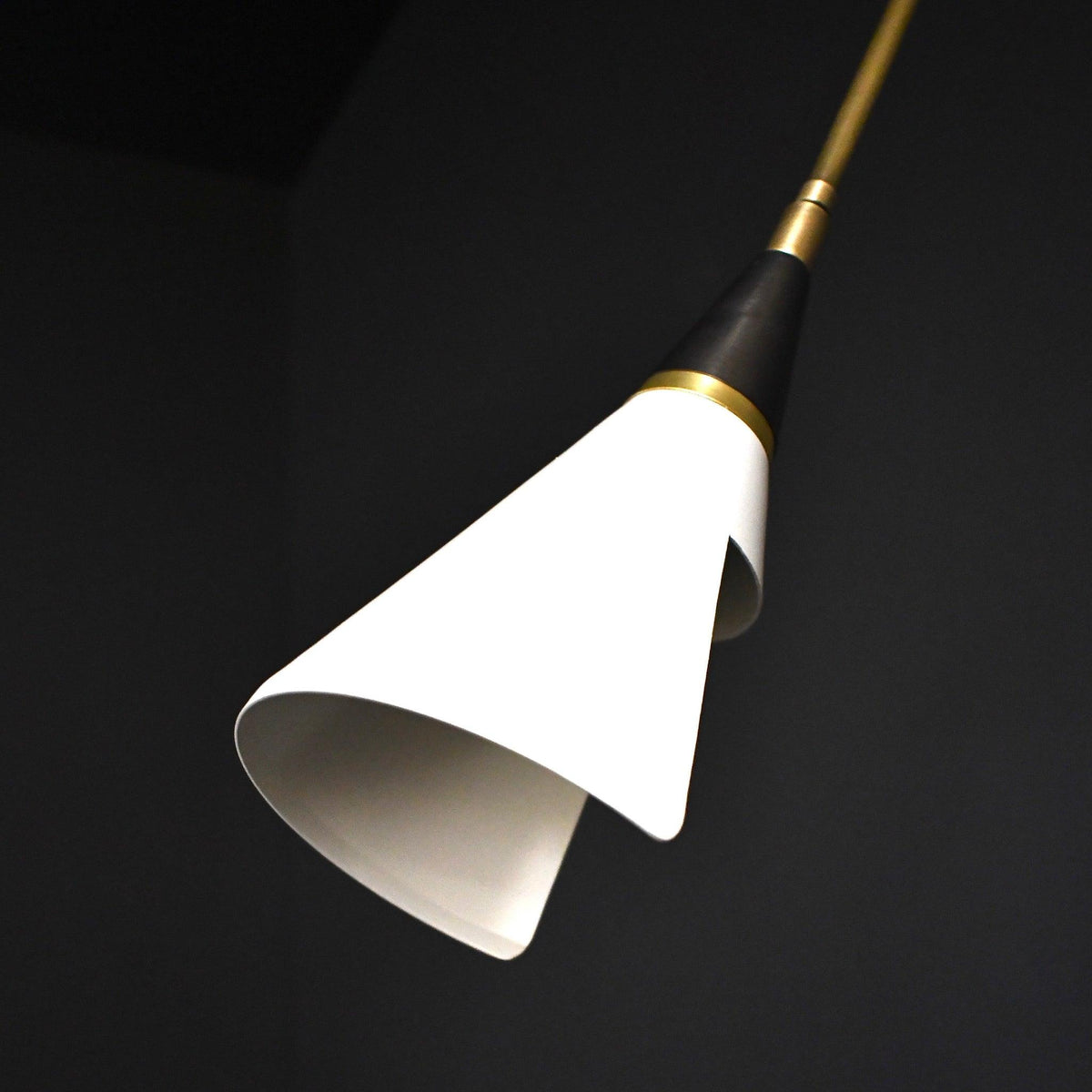 Close view of the white cone shade and black neck of this Clérachic wall light, on a dark backdrop with its lower rim curling inward.