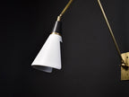 Close angle on a Clérachic wall light on a black backdrop, showing the white cone shade, the black neck and a brass collar.