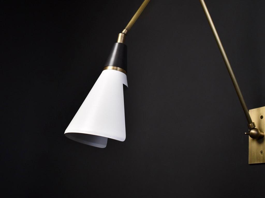 Close angle on a Clérachic wall light on a black backdrop, showing the white cone shade, the black neck and a brass collar.