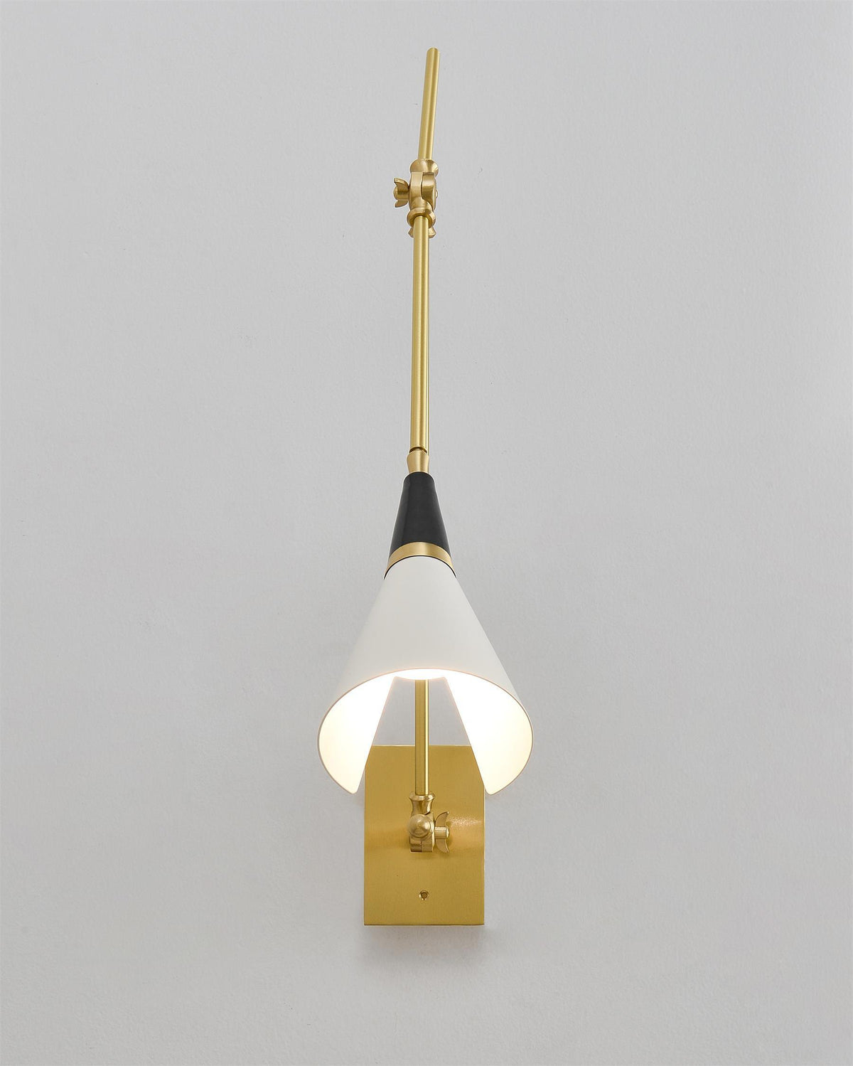 Front view of a Clérachic wall light with the arm raised straight, the white cone shade lit inside and a brass backplate at the base.