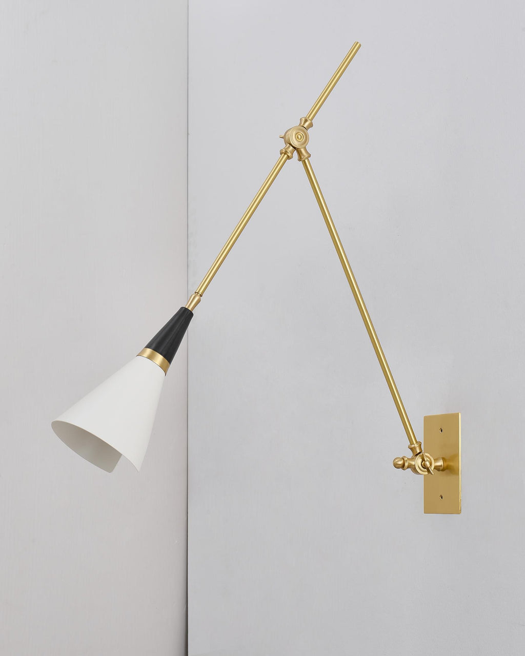 Clérachic wall light with a smaller white cone shade held low on its brass arm, on a pale wall meeting a corner.