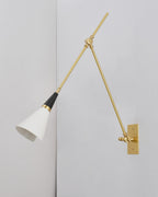Clérachic wall light with a smaller white cone shade held low on its brass arm, on a pale wall meeting a corner.