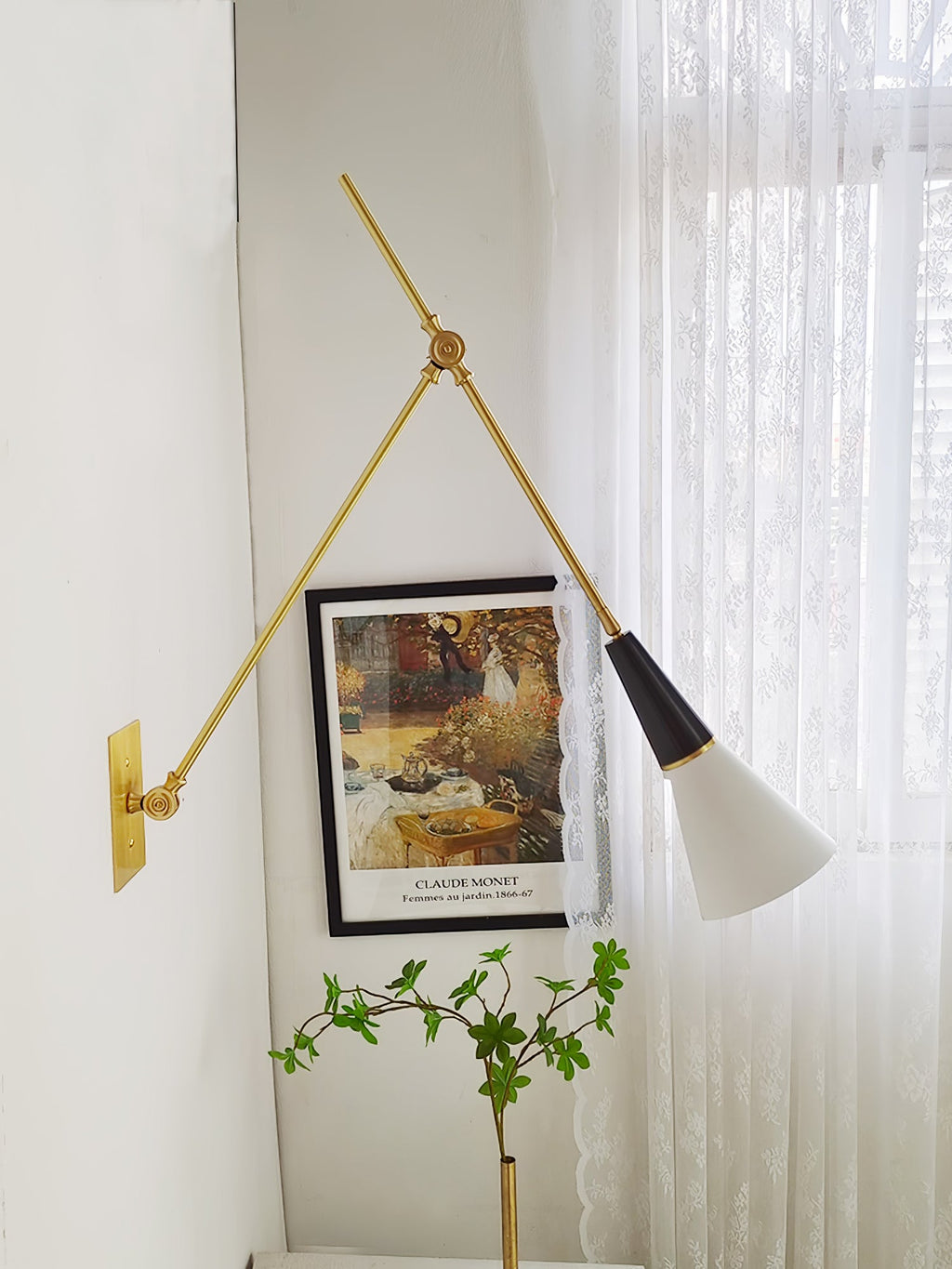 Clérachic wall light beside a framed garden print and a plant, with sheer lace curtains at the window and the arm angled out.